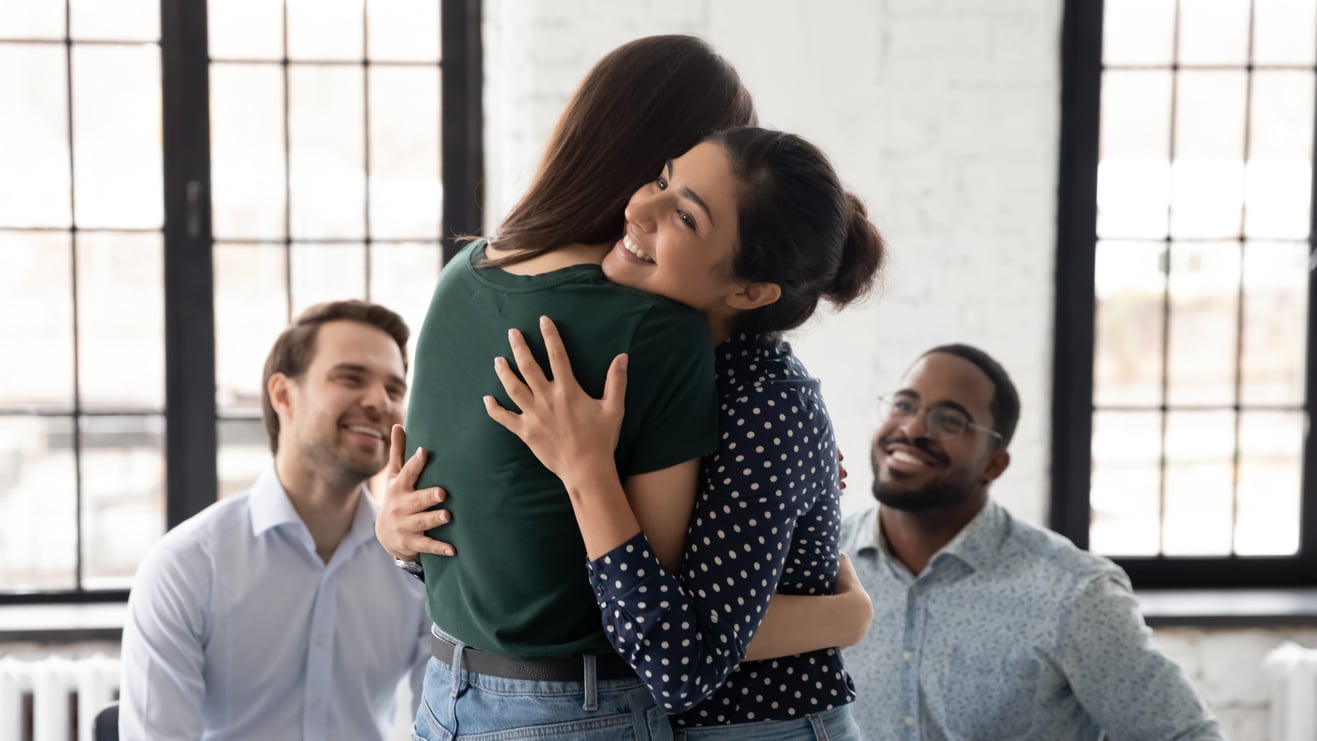 Smiling Indian psychologist hugging patient at group counselling session